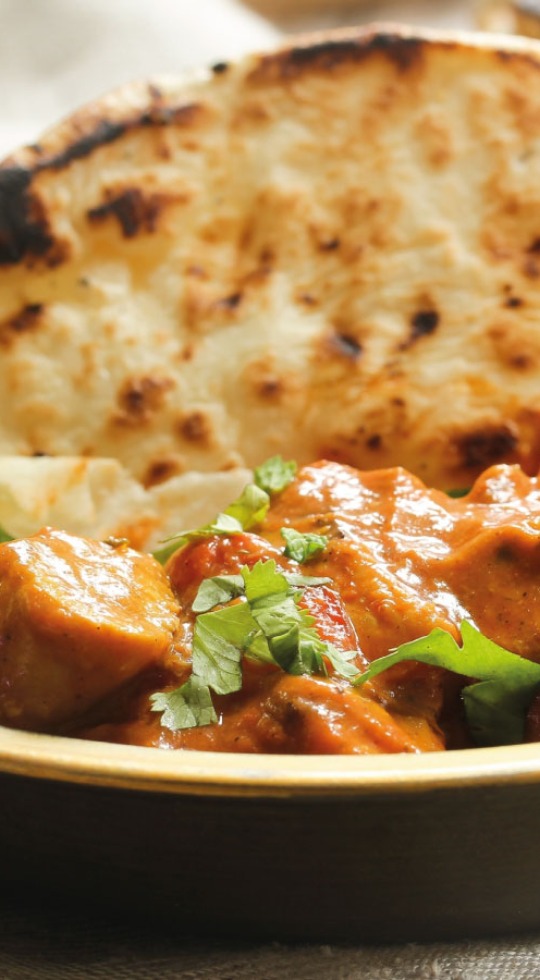 Close up of a bowl of curry with naan, garnished with coriander